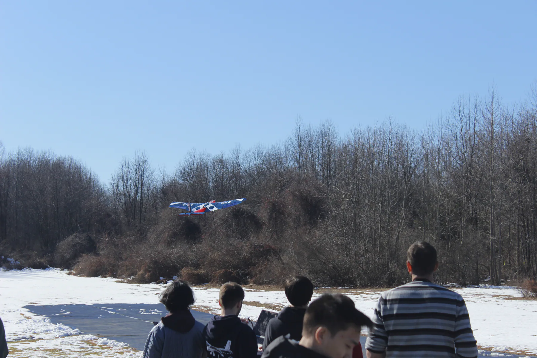 Leviathan flying above a snowy field while team members observe.